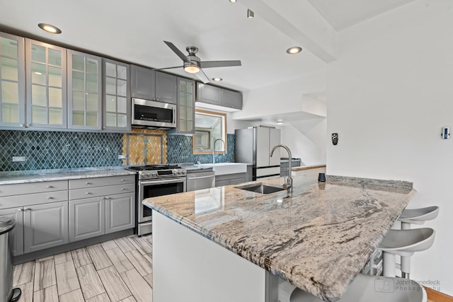 619 N 4th Ave, Maywood, IL 60153 - kitchen featuring appliances with stainless steel finishes, gray cabinetry, a peninsula, light stone countertops, and a kitchen breakfast bar