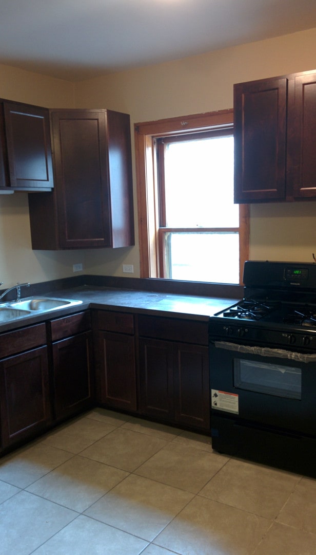 2244 W Augusta Blvd, Chicago, IL 60622 - kitchen with black range with gas cooktop, light tile patterned floors, dark brown cabinetry, and dark countertops