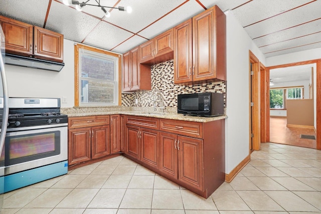 3545 W 62nd Pl, Chicago, IL 60629 - kitchen featuring stainless steel gas stove, black microwave, light tile patterned flooring, decorative backsplash, and brown cabinetry