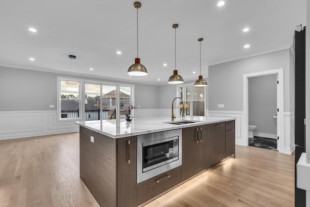 7635 W Balmoral Ave, Chicago, IL 60656 - kitchen with stainless steel microwave, dark brown cabinetry, a wainscoted wall, ornamental molding, and an island with sink