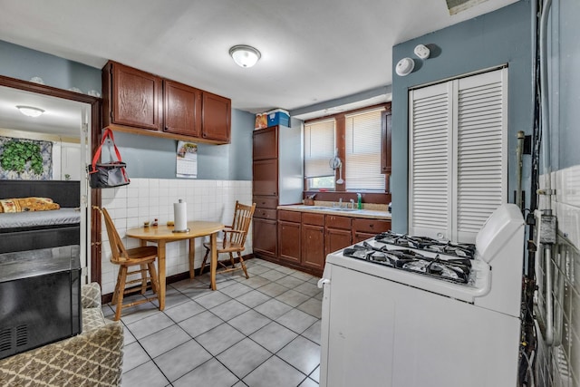 3031 S Central Park Ave, Chicago, IL 60623 - kitchen featuring white range with gas stovetop, light tile patterned flooring, tile walls, a wainscoted wall, and brown cabinetry