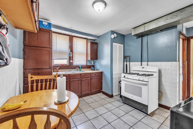 3031 S Central Park Ave, Chicago, IL 60623 - kitchen with white range with gas cooktop, tile walls, light tile patterned floors, light countertops, and a wainscoted wall