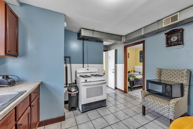 3031 S Central Park Ave, Chicago, IL 60623 - kitchen with white gas range, black microwave, light countertops, light tile patterned flooring, and tile walls