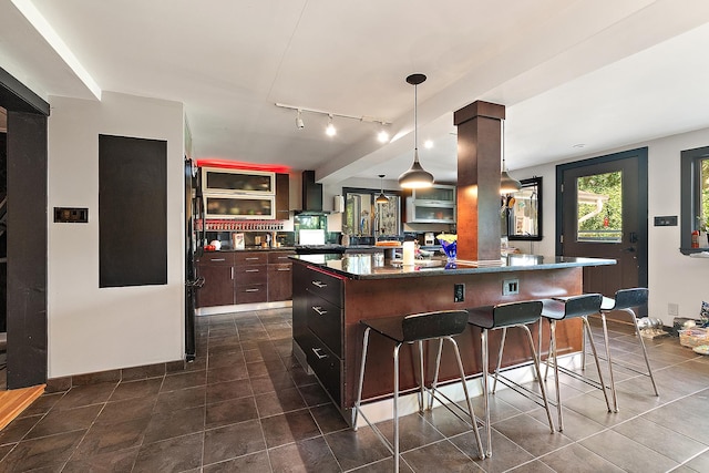 1108 Plaza Dr, New Lenox, IL 60451 - kitchen featuring dark countertops, wall chimney exhaust hood, a breakfast bar, a center island, and dark tile patterned flooring