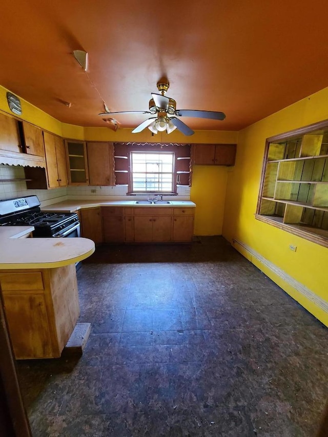 kitchen featuring gas range, light countertops, brown cabinetry, a peninsula, and ceiling fan
