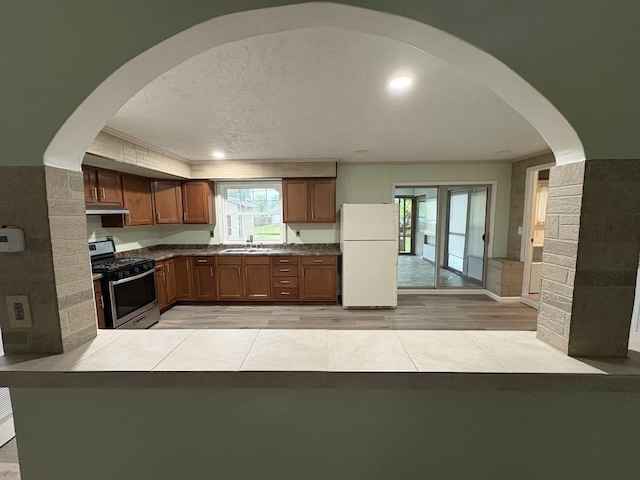 11071 E Fisher Rd, Rochelle, IL 60168 - kitchen with stainless steel range with gas cooktop, freestanding refrigerator, under cabinet range hood, light wood finished floors, and brown cabinets