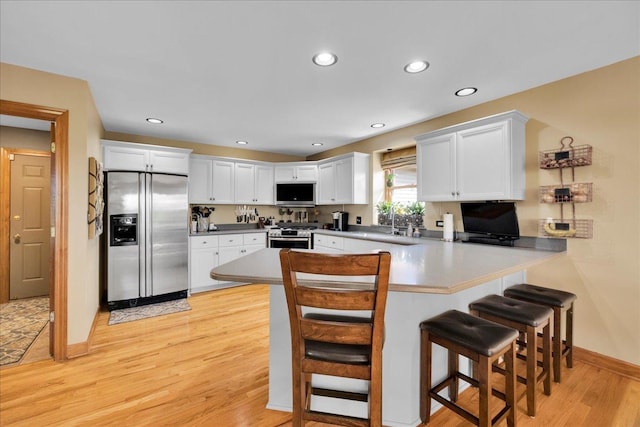 531 Danbury Dr, Oswego, IL 60543 - kitchen with appliances with stainless steel finishes, a peninsula, light wood finished floors, a kitchen breakfast bar, and white cabinetry