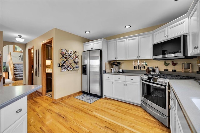 531 Danbury Dr, Oswego, IL 60543 - kitchen featuring appliances with stainless steel finishes, white cabinets, light wood-style flooring, arched walkways, and recessed lighting
