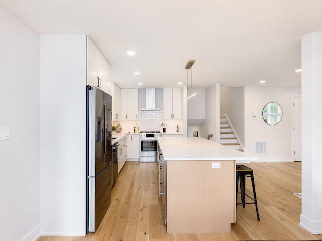 5028 Coyle Ave, Skokie, IL 60077 - kitchen featuring appliances with stainless steel finishes, wall chimney range hood, a kitchen breakfast bar, a kitchen island, and light wood-style floors