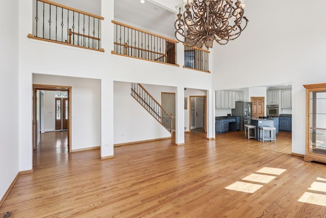 641 Mason Ln, Lake In The Hills, IL 60156 - unfurnished living room with a towering ceiling, light wood-type flooring, a chandelier, and stairs