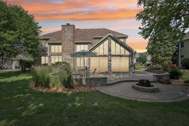 641 Mason Ln, Lake In The Hills, IL 60156 - back of property at dusk featuring a patio area, a fire pit, a yard, a chimney, and stone siding
