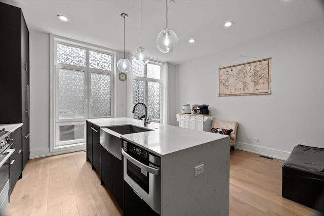 6223 S Ellis Ave, Chicago, IL 60637 - kitchen featuring dark cabinets, appliances with stainless steel finishes, light wood finished floors, an island with sink, and light countertops