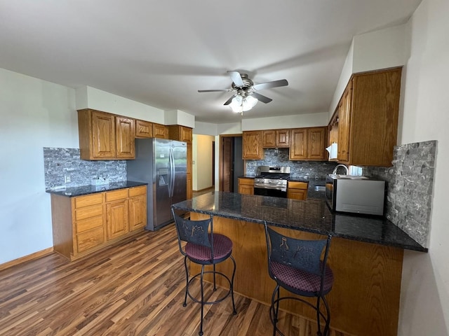 1536 Marberly Dr, Rockford, IL 61103 - kitchen featuring appliances with stainless steel finishes, a peninsula, tasteful backsplash, brown cabinetry, and dark wood-style flooring