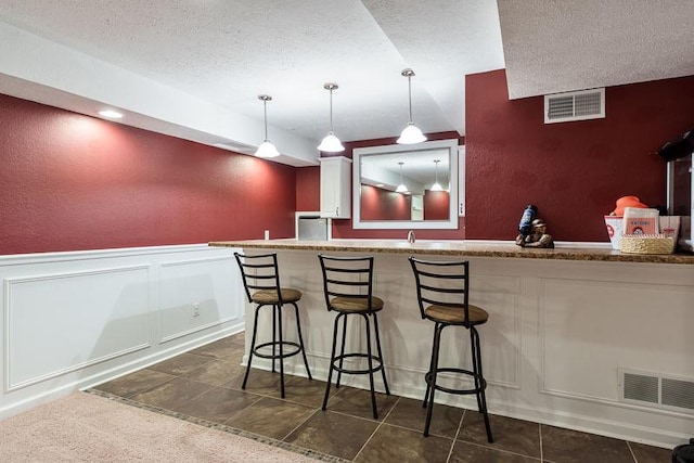 12499 Ayrshire Ln, Loves Park, IL 61111 - indoor wet bar with a textured ceiling, a decorative wall, hanging light fixtures, wainscoting, and a textured wall