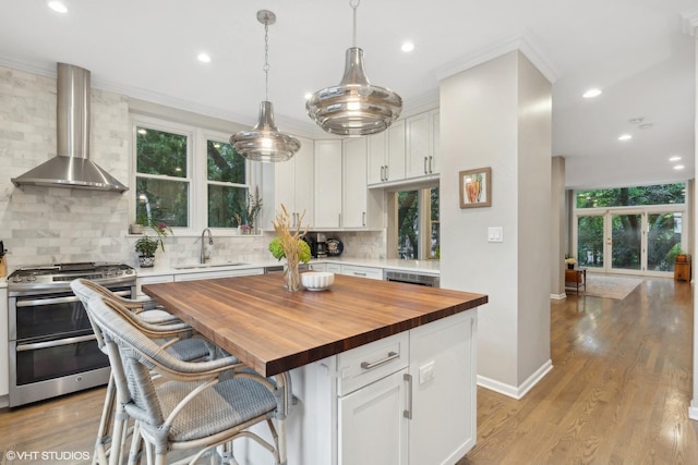 1212 W School St, Chicago, IL 60657 - kitchen with range with two ovens, wall chimney range hood, wooden counters, white cabinetry, and decorative backsplash