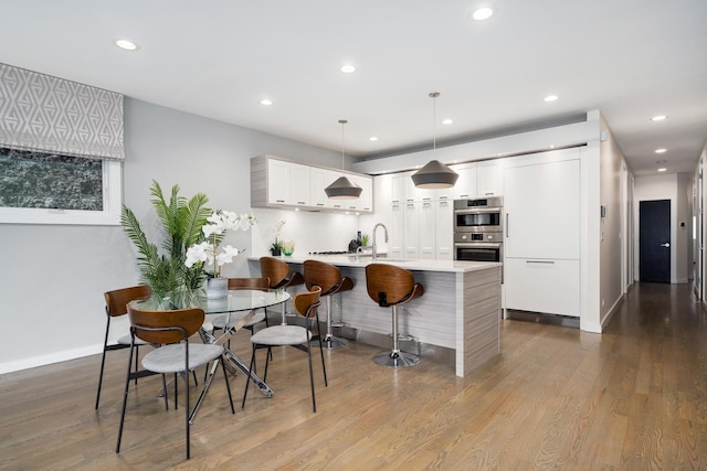 927 N Damen Ave Unit 2, Chicago, IL 60622 - kitchen featuring recessed lighting, stainless steel double oven, light countertops, dark wood-style flooring, and a breakfast bar area