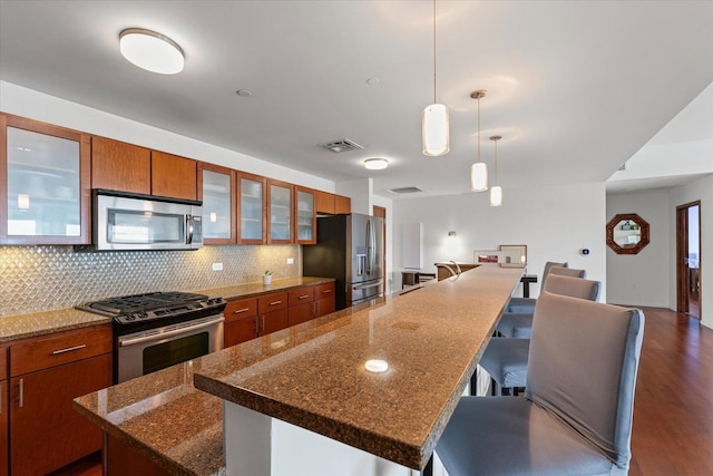 301 N Neil St Unit 609, Champaign, IL 61820 - kitchen featuring stainless steel appliances, brown cabinetry, tasteful backsplash, a kitchen bar, and glass insert cabinets