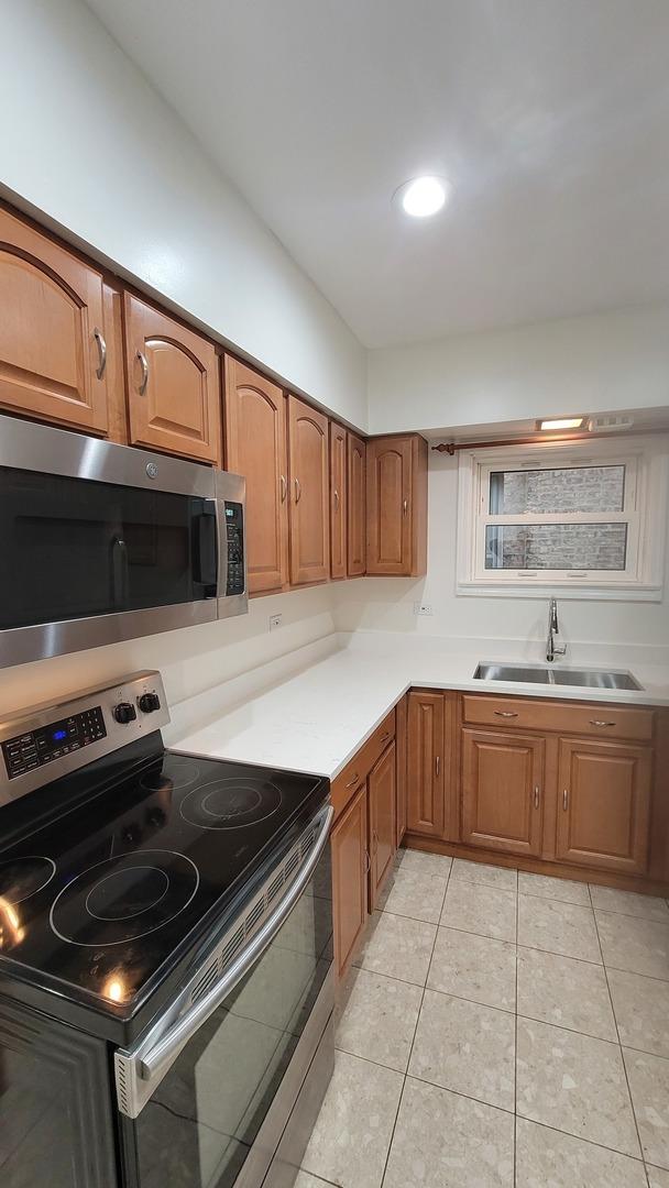 5448 W Agatite Ave, Chicago, IL 60630 - kitchen with stainless steel appliances, brown cabinetry, light tile patterned flooring, and light countertops