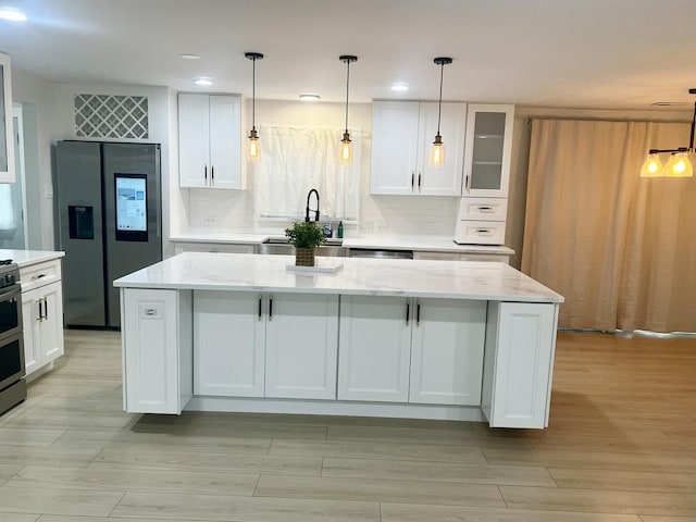 225 Webster Ln, Schaumburg, IL 60193 - kitchen featuring appliances with stainless steel finishes, white cabinetry, tasteful backsplash, a center island, and light stone counters