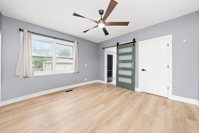 422 Locust St, Elgin, IL 60123 - unfurnished bedroom with a barn door, light wood-style floors, and ceiling fan