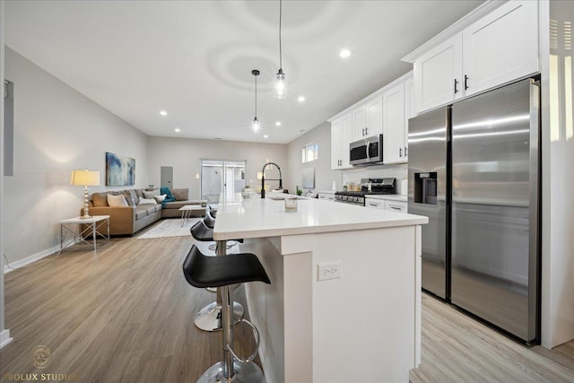 530 E 44th Pl, Chicago, IL 60653 - kitchen featuring appliances with stainless steel finishes, light wood-style floors, a breakfast bar, white cabinets, and an island with sink