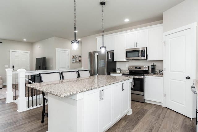 650 Anacostia Dr, Roscoe, IL 61073 - kitchen with appliances with stainless steel finishes, wood finished floors, a breakfast bar area, a kitchen island, and recessed lighting