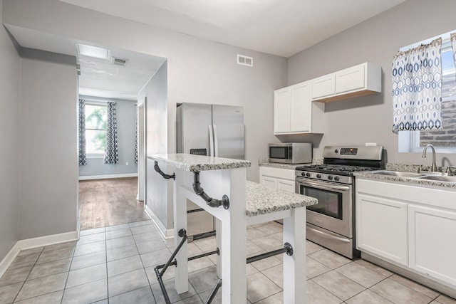 2630 S Spaulding Ave, Chicago, IL 60623 - kitchen with appliances with stainless steel finishes, white cabinetry, a kitchen bar, light tile patterned floors, and light stone counters