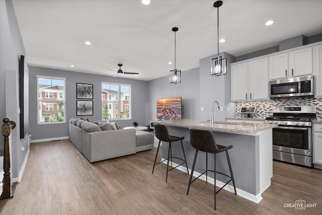 875 Finley Dr, Aurora, IL 60504 - kitchen featuring appliances with stainless steel finishes, wood finished floors, backsplash, a kitchen bar, and a kitchen island with sink