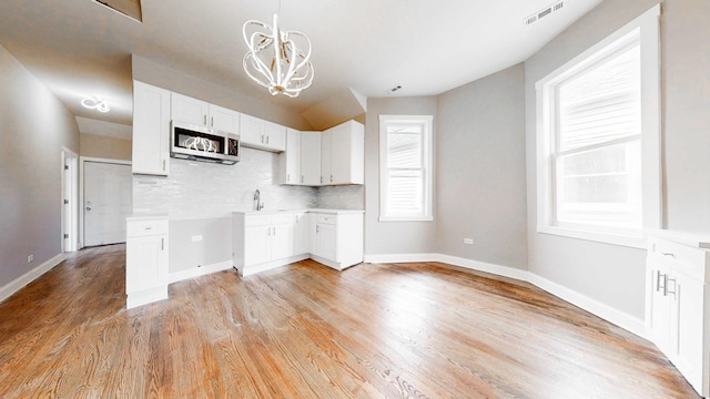 5915 S Sangamon St, Chicago, IL 60621 - kitchen with stainless steel microwave, a chandelier, white cabinets, backsplash, and light wood-style floors
