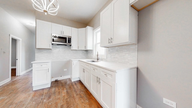 5915 S Sangamon St, Chicago, IL 60621 - kitchen with stainless steel microwave, decorative backsplash, white cabinetry, light wood finished floors, and a chandelier