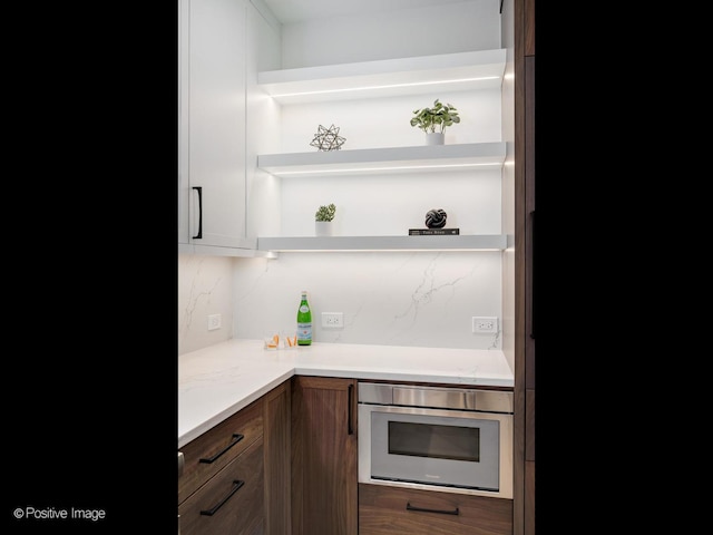 2841 N Southport Ave Unit 2, Chicago, IL 60657 - kitchen with open shelves, stainless steel microwave, decorative backsplash, and light stone counters