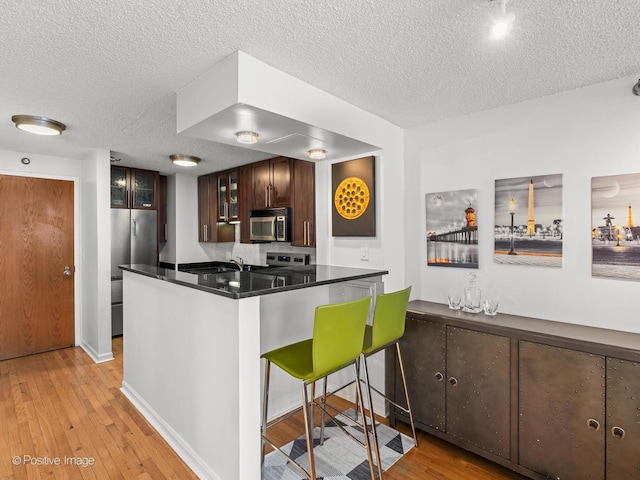1122 N Clark St Unit 2609, Chicago, IL 60610 - kitchen with stainless steel appliances, a textured ceiling, glass insert cabinets, light wood-style flooring, and dark brown cabinets