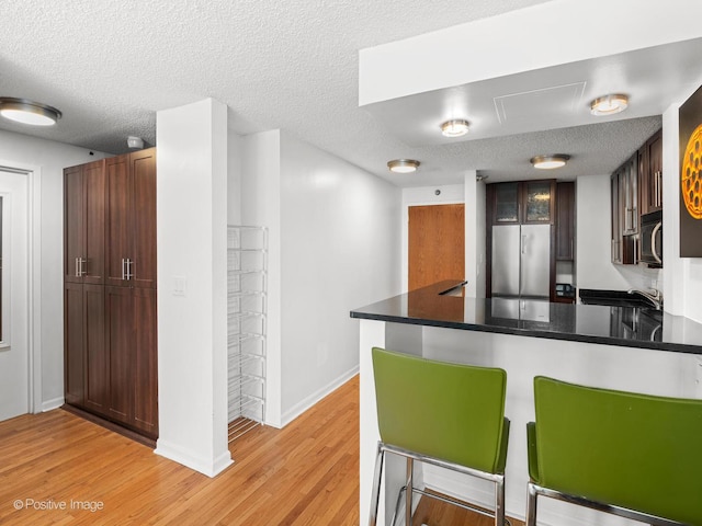 1122 N Clark St Unit 2609, Chicago, IL 60610 - kitchen with stainless steel refrigerator, a peninsula, light wood-style floors, a kitchen breakfast bar, and a textured ceiling