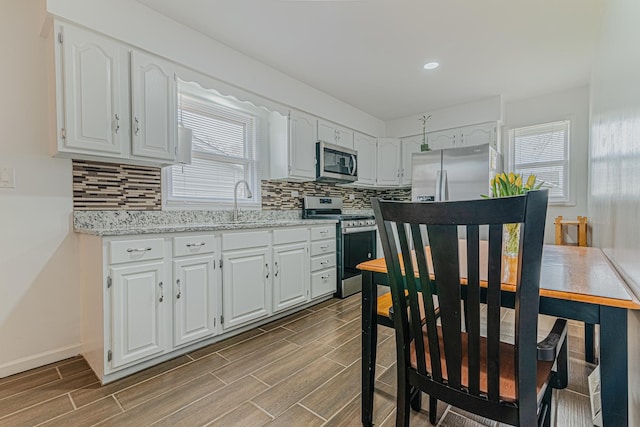 2105 Prospect Ave, North Chicago, IL 60064 - kitchen featuring appliances with stainless steel finishes, white cabinets, wood tiled floors, decorative backsplash, and healthy amount of natural light