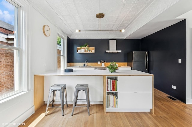 1510 W Cullerton St, Chicago, IL 60608 - kitchen featuring freestanding refrigerator, wall chimney exhaust hood, light wood finished floors, light countertops, and a peninsula