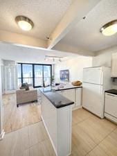 10 E Ontario St Unit 3912, Chicago, IL 60611 - kitchen with freestanding refrigerator, white cabinetry, dark countertops, light tile patterned floors, and beamed ceiling