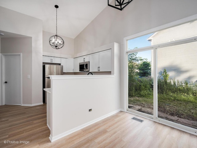 2804 River Bend Ln, Plainfield, IL 60586 - kitchen featuring stainless steel appliances, high vaulted ceiling, light wood-style floors, white cabinetry, and decorative light fixtures