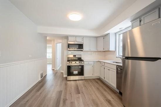 3131 N Odell Ave, Chicago, IL 60707 - kitchen with appliances with stainless steel finishes, light wood-type flooring, light countertops, and a wainscoted wall