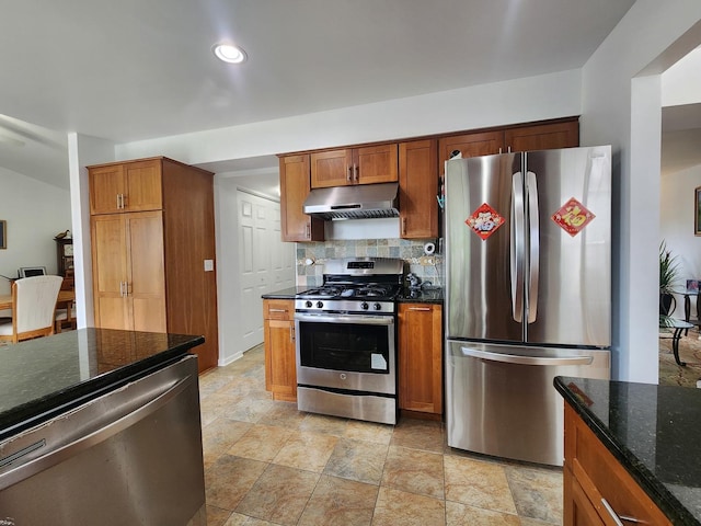 72 Wilton Ln, Mundelein, IL 60060 - kitchen featuring appliances with stainless steel finishes, under cabinet range hood, decorative backsplash, dark stone counters, and brown cabinets