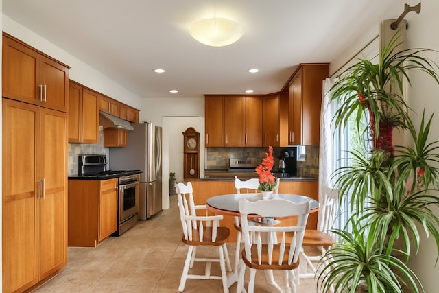 72 Wilton Ln, Mundelein, IL 60060 - kitchen featuring appliances with stainless steel finishes, under cabinet range hood, tasteful backsplash, light tile patterned floors, and dark countertops