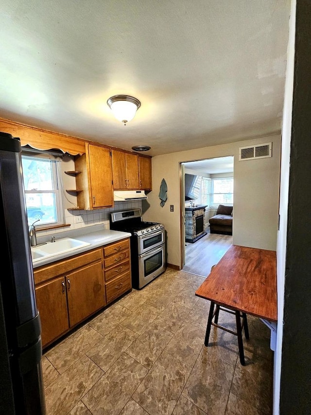 129 S Commonwealth Ave, Elgin, IL 60123 - kitchen with appliances with stainless steel finishes, brown cabinetry, healthy amount of natural light, and under cabinet range hood