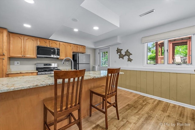 404 Kensington Dr, Mchenry, IL 60050 - kitchen with appliances with stainless steel finishes, light wood-type flooring, light stone counters, a kitchen bar, and a wainscoted wall