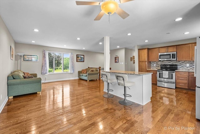 404 Kensington Dr, Mchenry, IL 60050 - kitchen with stainless steel appliances, open floor plan, brown cabinets, a kitchen breakfast bar, and light wood-style flooring