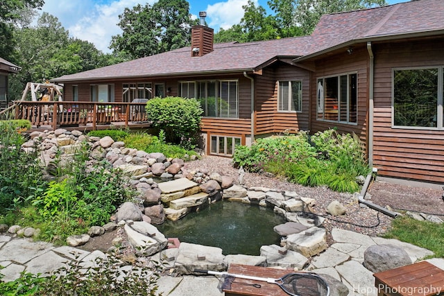 24099 W Haidi Ln, Lake Villa, IL 60046 - rear view of house featuring a chimney, a deck, a small pond, and roof with shingles