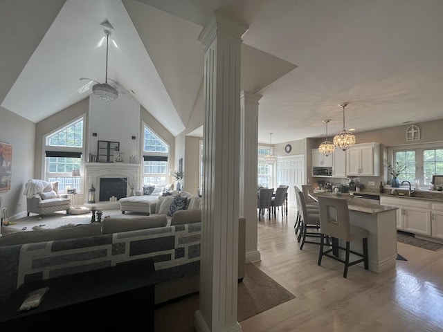 12534 Lily Ln, Plainfield, IL 60585 - living area with decorative columns, light wood-style floors, a fireplace, a chandelier, and vaulted ceiling