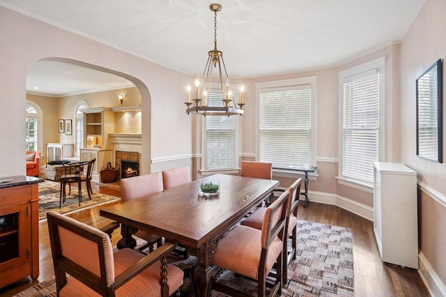 611 Lake Ave, Wilmette, IL 60091 - dining area with arched walkways, a tiled fireplace, dark wood finished floors, a chandelier, and crown molding