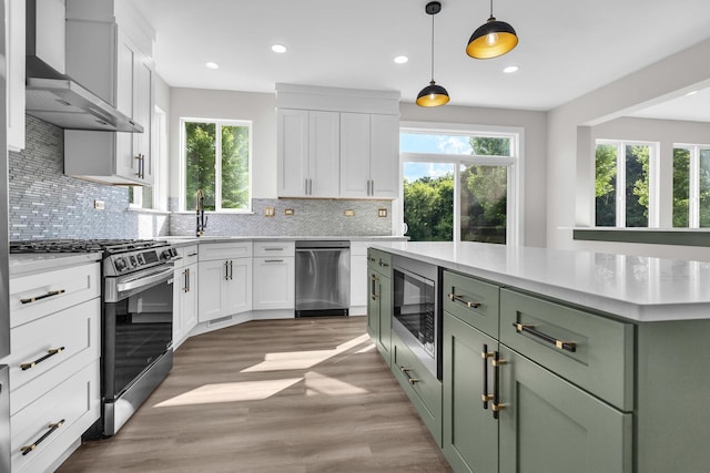 2054 S Jonathan Dr, Round Lake, IL 60073 - kitchen featuring appliances with stainless steel finishes, green cabinetry, wall chimney exhaust hood, healthy amount of natural light, and recessed lighting