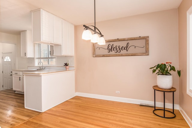 3345 N Page Ave, Chicago, IL 60634 - kitchen featuring light wood-type flooring, white cabinets, light countertops, a peninsula, and pendant lighting