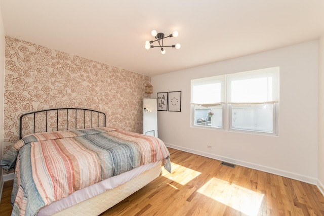 3345 N Page Ave, Chicago, IL 60634 - bedroom featuring wallpapered walls, wood finished floors, a chandelier, and an accent wall