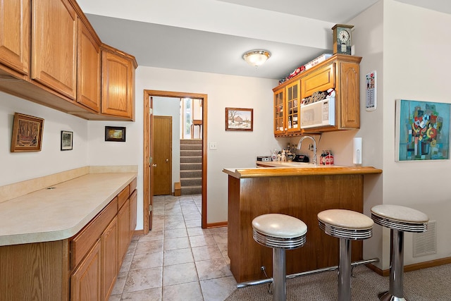 7672 Thistlewood Ln, Frankfort, IL 60423 - kitchen with white microwave, a breakfast bar, a peninsula, brown cabinets, and glass insert cabinets